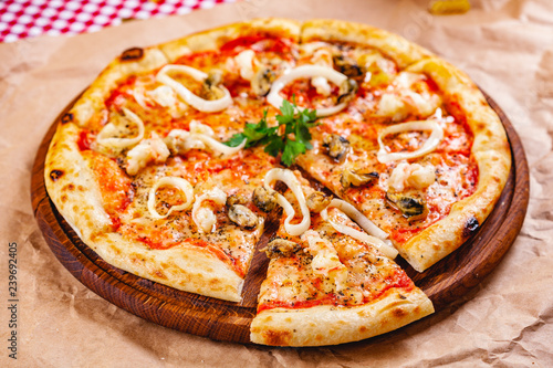 Italian Pizza with seafood and mozzarella cheese on wooden cutting board. Close up