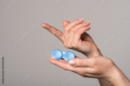 Soft contact lens and blue container in female hands on gray background