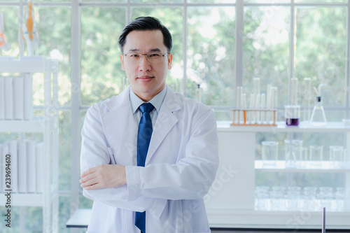A middle aged man scientist smiling happily with his arms crossed posing at her laboratory colleagues. A confident professor CEO standing preparing equipment for teaching collage student. Copy space.
