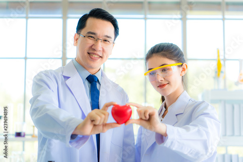 Portrait of man and woman doctors smiling in laboratory of hospital. Asian science hold red heart sharp symbol together. Hand hold ball. Science and health care concept. Soft and clean tone filter.