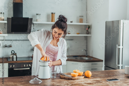 smiling girl making fresh orange juice with juicer at wooden table in kitchen photo