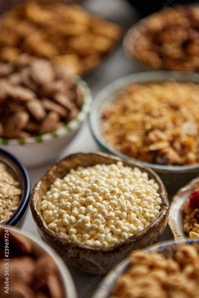 Close up and selective focus. Composition of different kinds cereals placed in ceramic bowls with cornflakes, granola, cereals and oatmeal. Flat lay, top view on white wooden table. Close up and selective focus. Composition of different kinds cereals placed in ceramic bowls with cornflakes, granola, cereals and oatmeal. Flat lay, top view on white wooden table.