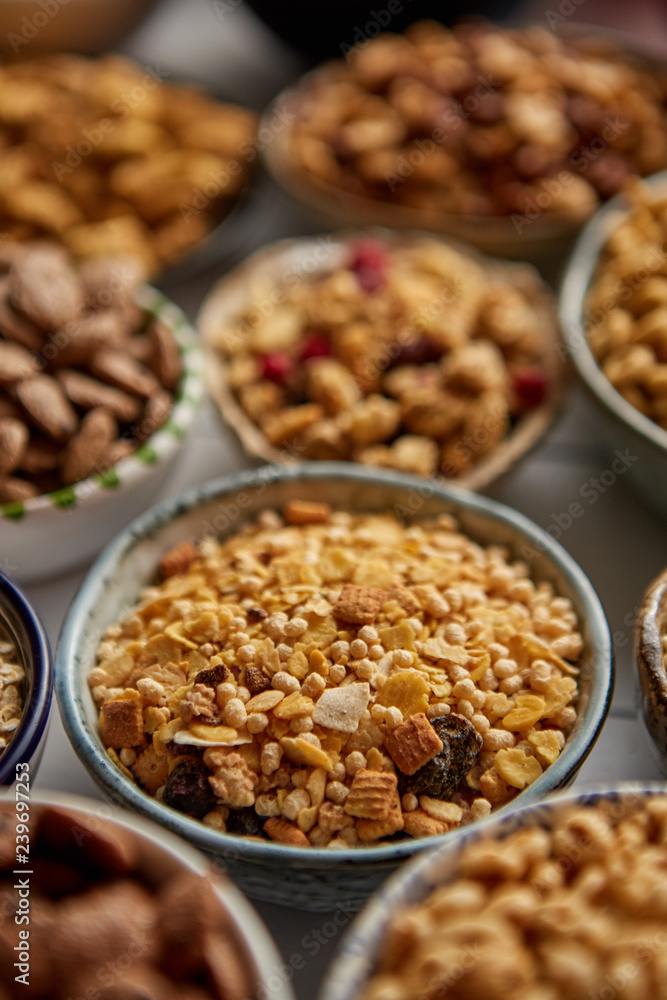 Close up and selective focus. Composition of different kinds cereals placed in ceramic bowls with cornflakes, granola, cereals and oatmeal. Flat lay, top view on white wooden table. Close up and selective focus. Composition of different kinds cereals placed in ceramic bowls with cornflakes, granola, cereals and oatmeal. Flat lay, top view on white wooden table.