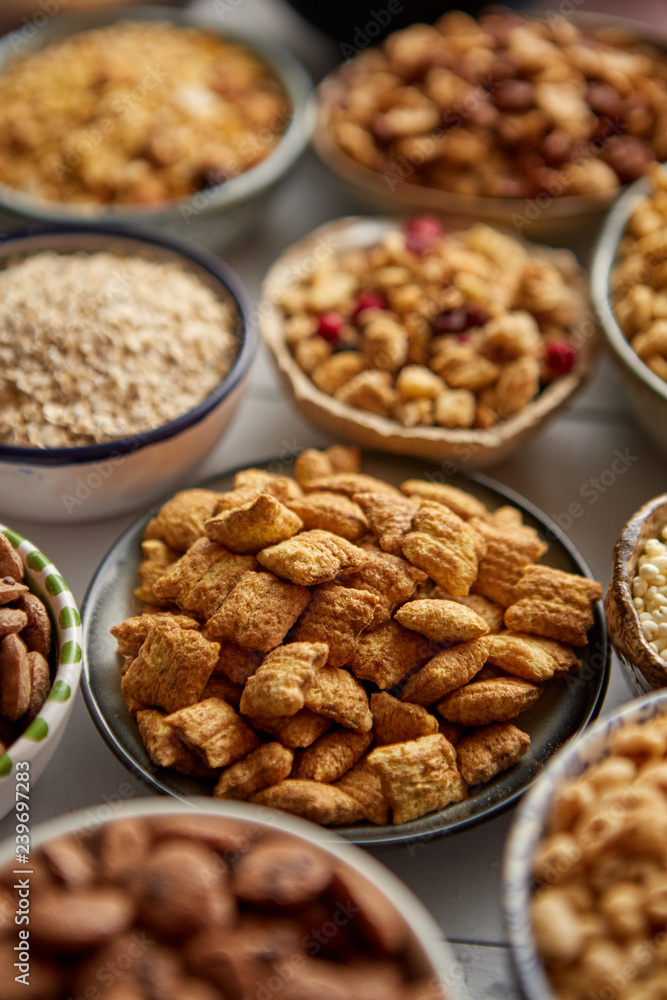 Close up and selective focus. Composition of different kinds cereals placed in ceramic bowls with cornflakes, granola, cereals and oatmeal. Flat lay, top view on white wooden table. Close up and selective focus. Composition of different kinds cereals placed in ceramic bowls with cornflakes, granola, cereals and oatmeal. Flat lay, top view on white wooden table.