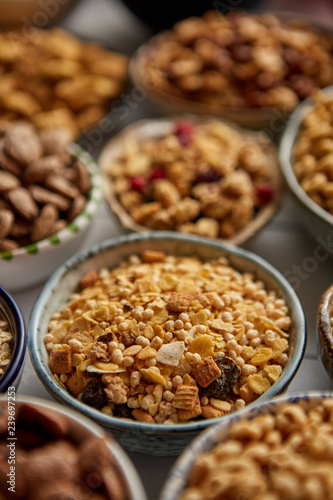 Close up and selective focus. Composition of different kinds cereals placed in ceramic bowls with cornflakes, granola, cereals and oatmeal. Flat lay, top view on white wooden table.