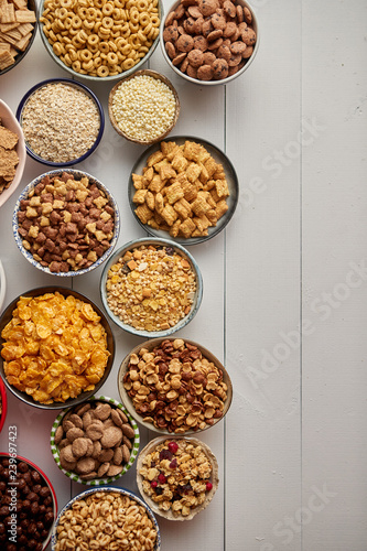 Assortment of different kinds cereals placed in ceramic bowls with cornflakes, granola, cereals and oatmeal. The concept of breakfast food. Flat lay, with copy space, top view on white wooden table.