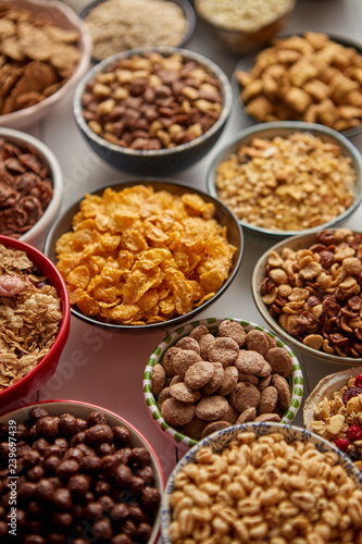 Assortment of different kinds cereals placed in ceramic bowls with cornflakes, granola, cereals and oatmeal. The concept of breakfast food. Flat lay, top view on white wooden table. © Dash
