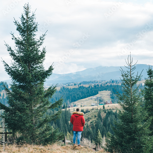 man in red coat standing at the cliff with beautiful mountains view