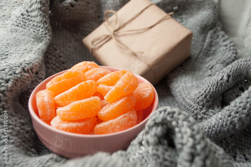 Flat lay of pink bowl full of peeled sweet tangerines on grey background with wraped giftbox.