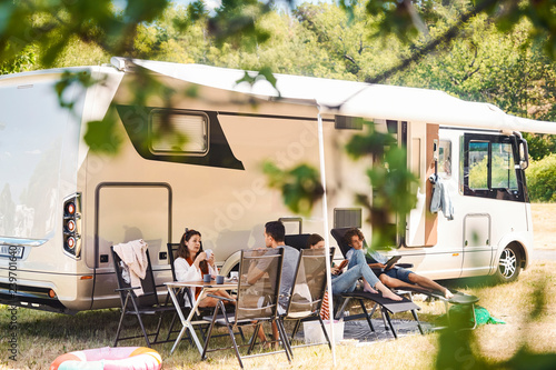 Family relaxing on chairs outside camper van at campsite during summer vacation photo