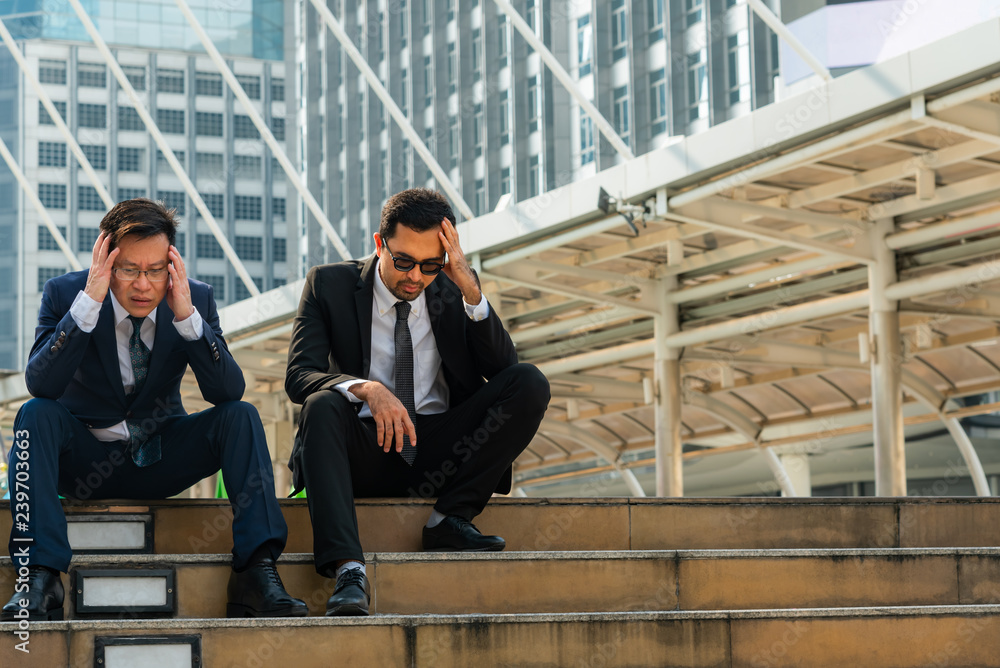 Asian business man sitting on a staircase between a tall building, stressed and fear by a business problem, Unsuccessful and unemployed, to strain concept. Asian business man sitting on a staircase between a tall building, stressed and fear by a business problem, Unsuccessful and unemployed, to strain concept.