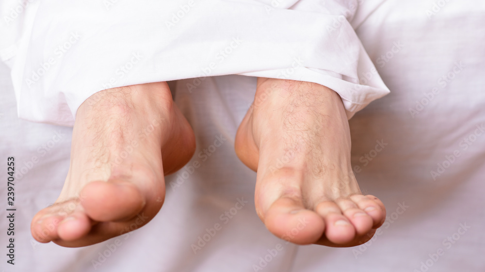 Man sleeping on bed under blanket. Sleep alone. Healthy skin on foot. Size of foot. Male feet on bed in morning. Fresh and relaxed. Health and wellbeing concept. Feet appear out of blanket close up Man sleeping on bed under blanket. Sleep alone. Healthy skin on foot. Size of foot. Male feet on bed in morning. Fresh and relaxed. Health and wellbeing concept. Feet appear out of blanket close up