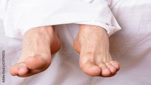 Man sleeping on bed under blanket. Sleep alone. Healthy skin on foot. Size of foot. Male feet on bed in morning. Fresh and relaxed. Health and wellbeing concept. Feet appear out of blanket close up