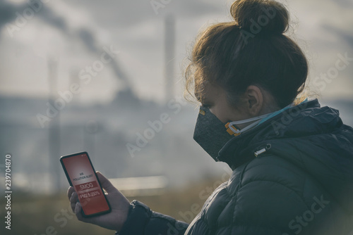 Plakat Kobieta ubrana w prawdziwą antysmogową maskę i sprawdzająca aktualne zanieczyszczenie powietrza dzięki aplikacji na smartfony
