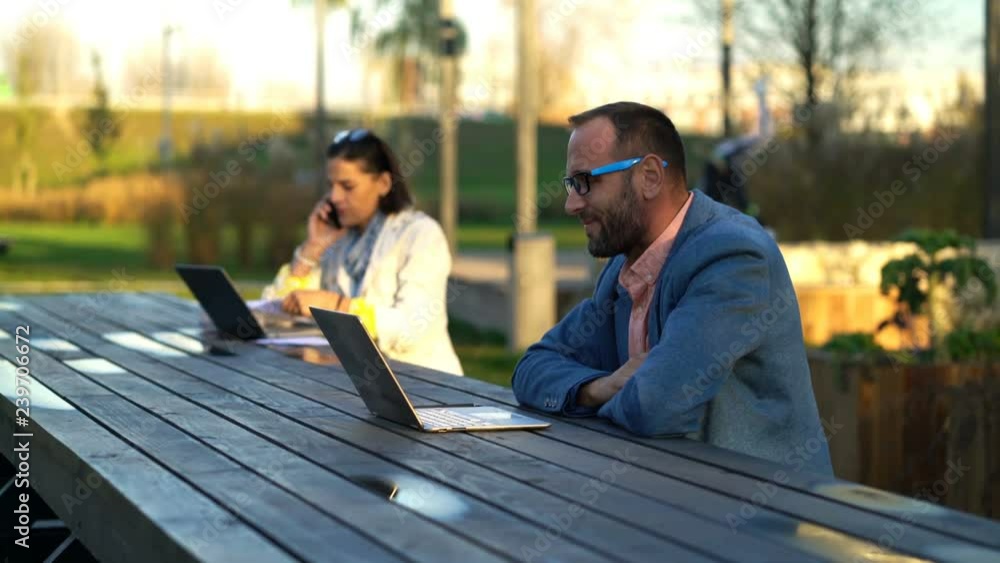 Young businessman watching movie on laptop by table at city park Young businessman watching movie on laptop by table at city park