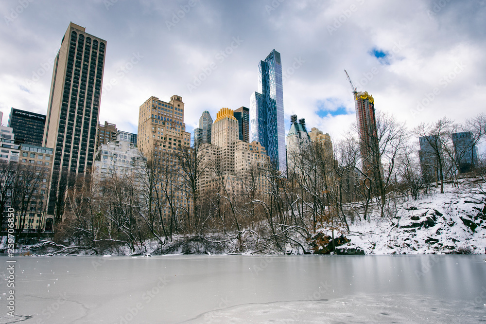 Overcast view of the Midtown Manhattan skyline towering over the ice of the frozen Central Park pond on a cold winter morning in New York City