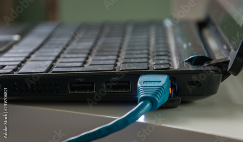  Blue ethernet cable connected to a black laptop on a white table. The lights near the cable head are on.