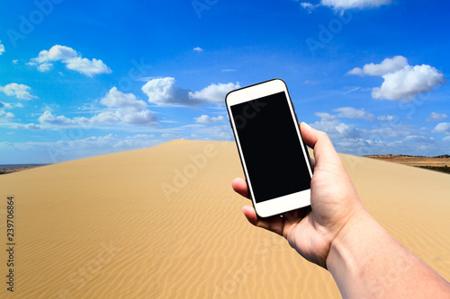 Hand holding blank screen smartphone with beautiful sky and sand dune in desert with copy space.