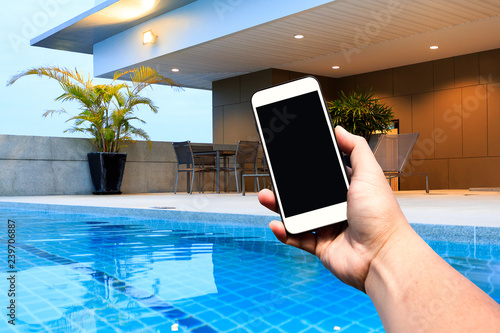 Hand hold Modern smartphone with blank screen at outdoor swimming pool and terrace upper deck. Copy space.