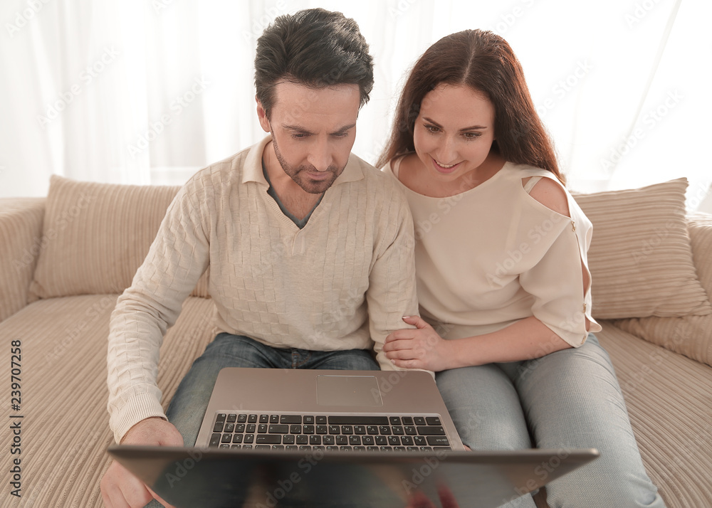 couple with laptop sitting in the living room on the sofa