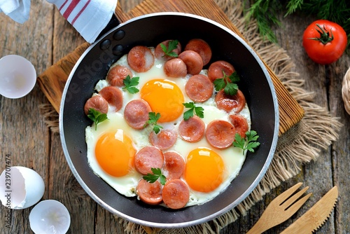 Homemade fried eggs with sausages in a frying pan on wooden background. Classic breakfast. Top view.