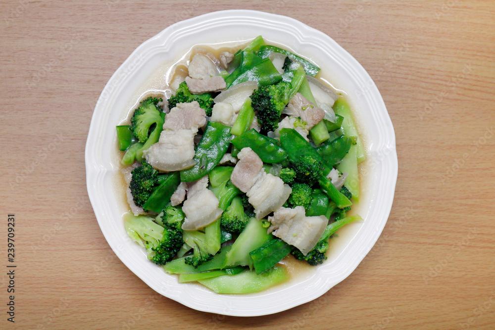 Stir Fried Broccoli, Peas with Crispy Pork with oyster sauce, Fried vegetable broccoli for food menu diet healthy in a dish on a wooden floor (Thai Foods) Stir Fried Broccoli, Peas with Crispy Pork with oyster sauce, Fried vegetable broccoli for food menu diet healthy in a dish on a wooden floor (Thai Foods)
