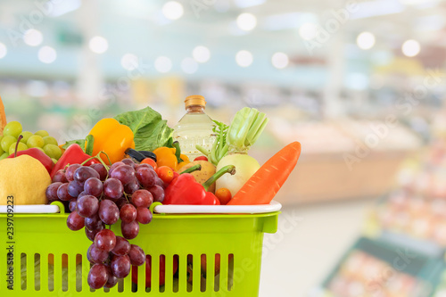 Shopping basket filled with fruits and vegetables with supermarket grocery store blurred defocused background with bokeh light