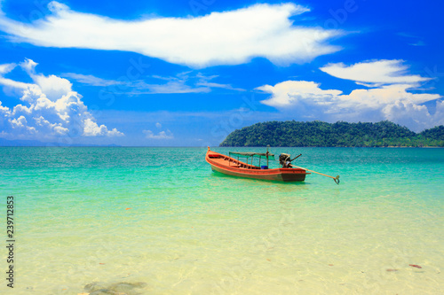 A fishing boat floating on beach with clean and clear sea and cloudy blue sky. Copy space. 