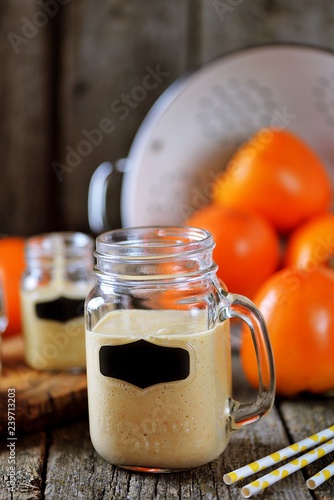 Healthy persimmon smoothie with banana and yogurt on wooden background.