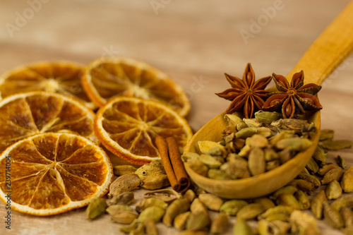 Fototapeta Naklejka Na Ścianę i Meble -  Pile of aromatic cardamom and spicy star anise in wooden spoon arranged on table with sweet dried oranges for Christmas Day