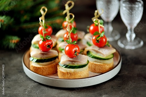 Canape with salted herring, cucumber, boiled potatoes and cherry tomato on rye croutons. Christmas background.