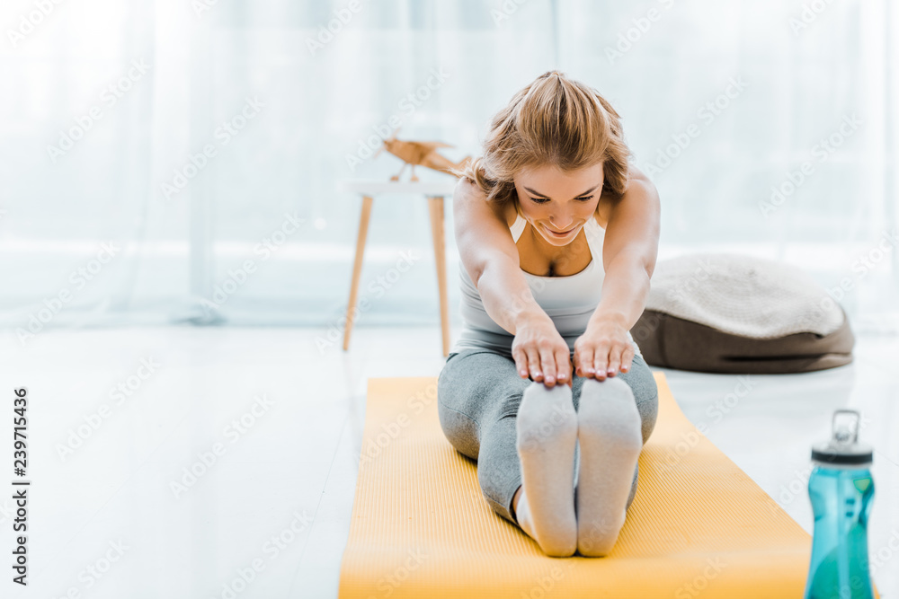 woman in sportswear doing stretching exercise on yellow fitness mat in living room