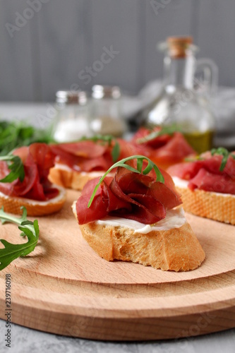 Canape or crostini with toasted baguette, light cheese, bresaola and arugula on wooden board. Diet food. Iron food. photo