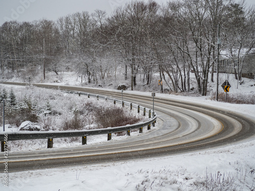 Slippery bend in the road on an overcast winters day, tire tracks, guardrail, snowing.