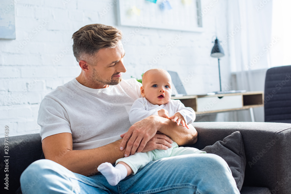 handsome smiling father sitting on sofa and holding adorable baby daughter at home handsome smiling father sitting on sofa and holding adorable baby daughter at home