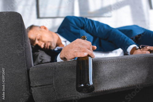 selective focus of bottle in hand of drunk businessman sleeping on sofa © LIGHTFIELD STUDIOS