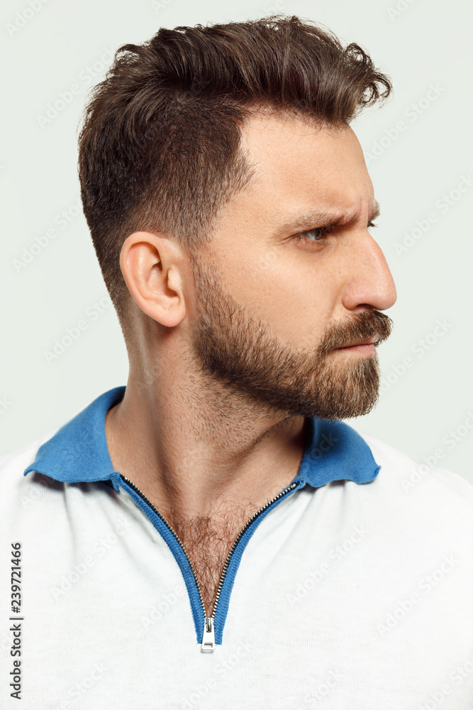 Obraz premium Serious man standing, looking at camera isolated on white studio background. Beautiful, young face. male half-length portrait. Human emotions, facial expression concept.