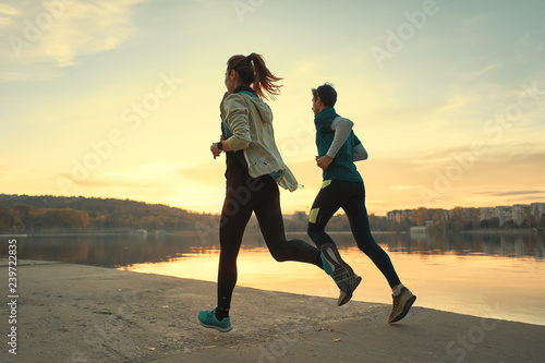 Young man and woman out for a run on the lake at the sunrise
