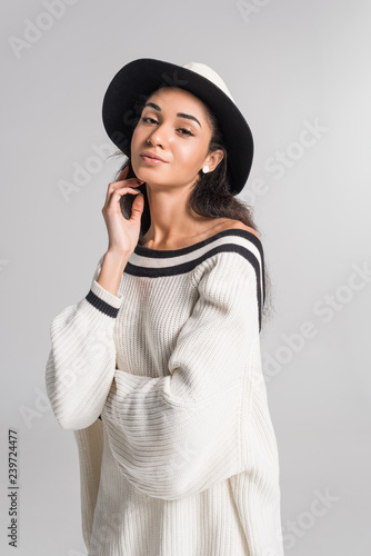 beautiful cheerful african american girl in stylish white sweater and hat posing isolated on white