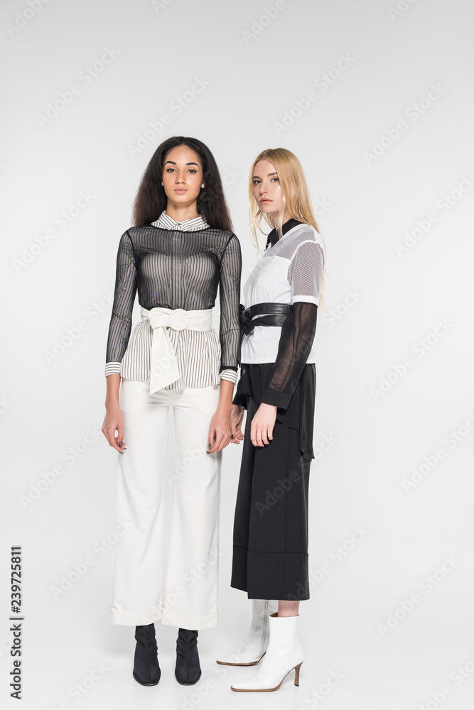 beautiful multicultural women in fashionable black and white clothes looking at camera isolated on white beautiful multicultural women in fashionable black and white clothes looking at camera isolated on white