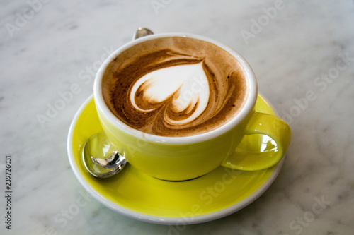 Capuccino coffer with foam heart in yellow cup on marble surface