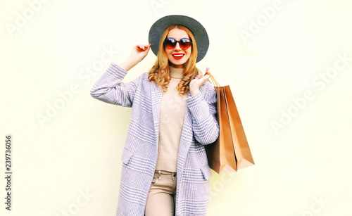 Beautiful young smiling woman with shopping bags in pink coat, round hat on wall background