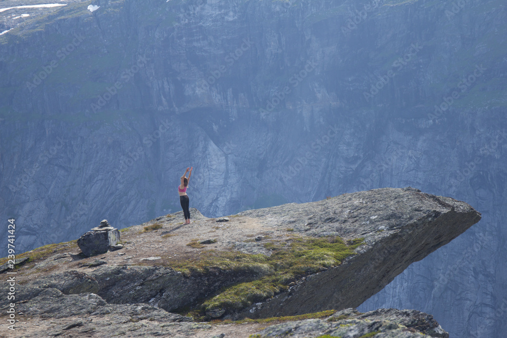 20 July 2017: Happy young woman doing exercises, doing yoga, on a mountain near the Trolltunga. The summer trip to Trolltunga hiking route. The Troll's tongue, in Odda Ringedalsvatnet lake, Norway.