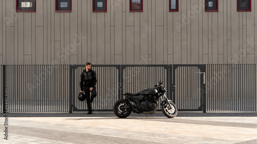 Handsome guy rider with a beard and mustache, stands near the wall of the fence. Bicycle to order in a vintage garage. Brutal urban lifestyle photo