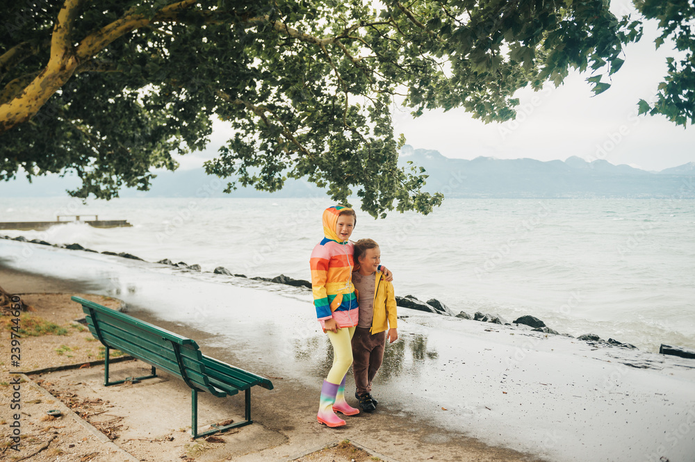 Group of two funny kids playing by the lake on a very windy day, watching  waves, wearing rain coats. Image taken on lake Geneva, Lausanne, Switzerland  Stock Photo | Adobe Stock