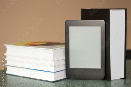 Modern e-book on the background of a stack of thick paper books. Close-up with selective focus. Training and technology concept photo