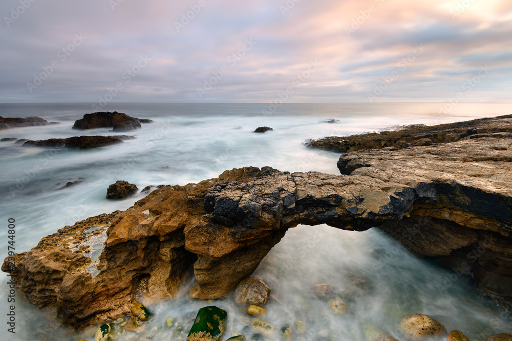 Seascape in Cascais Portugal. Stone bridge carved by the tides. Coastal landscape near Lisbon. Long exposure on a stormy day.