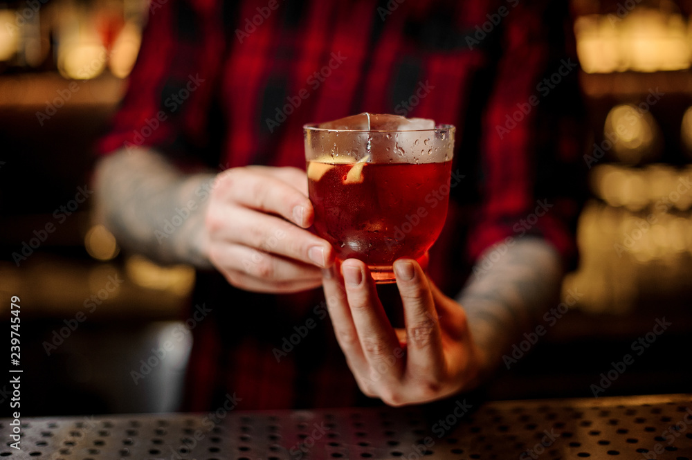 Bartender holding a strong alcoholic drink with whiskey and orange peel