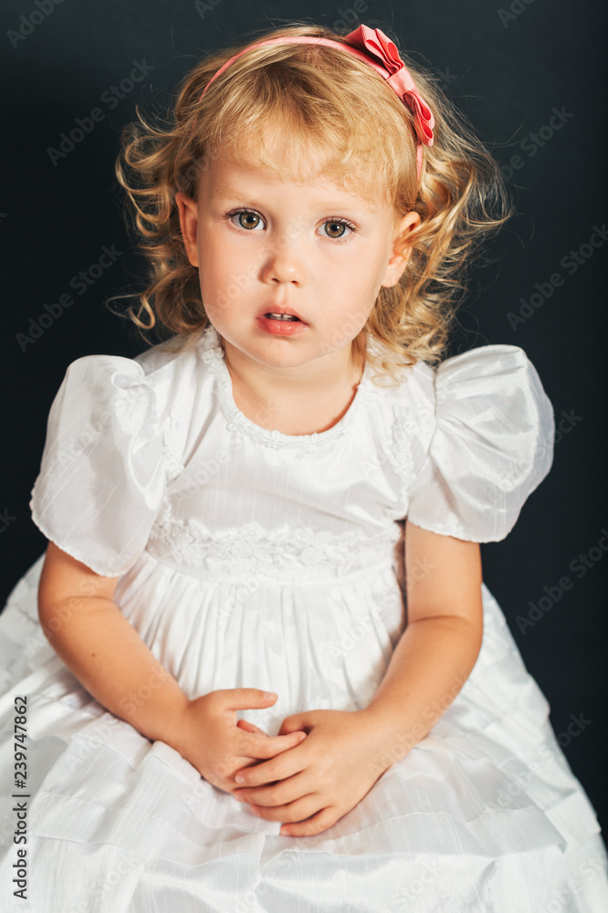Studio shot of adorable 3 year old toddler girl wearing white occasion dress Studio shot of adorable 3 year old toddler girl wearing white occasion dress