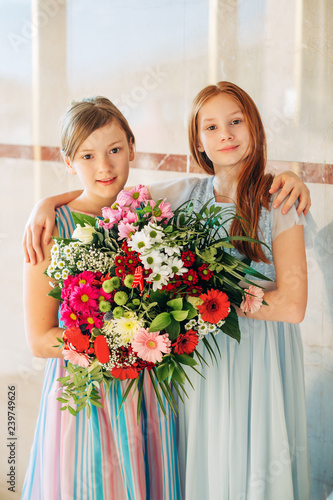 Two beautiful girls wearing occasion dresses, holding big flower bouquet